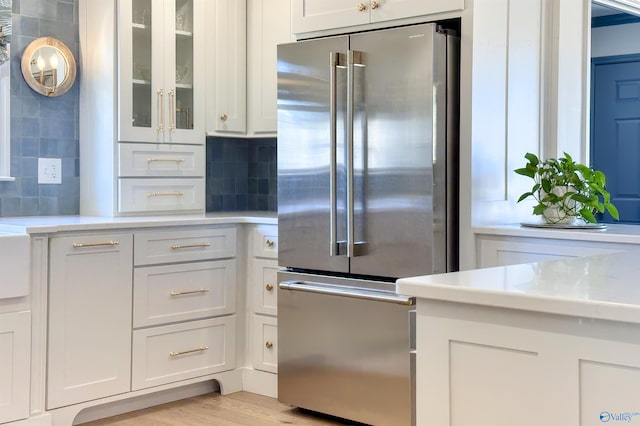 kitchen with white cabinetry, high end refrigerator, light wood-type flooring, and backsplash