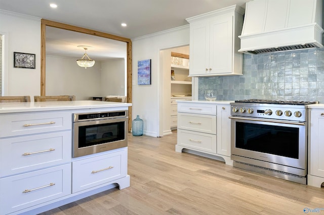 kitchen with appliances with stainless steel finishes, pendant lighting, tasteful backsplash, white cabinets, and custom range hood