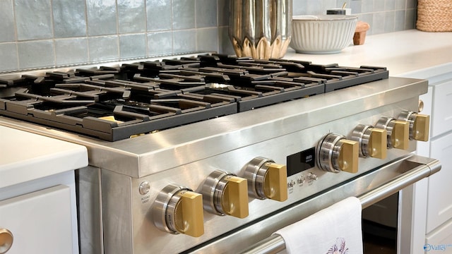 interior details with tasteful backsplash, stainless steel range, and white cabinets