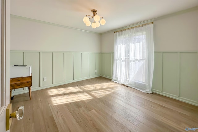 empty room with a notable chandelier, crown molding, and light hardwood / wood-style floors