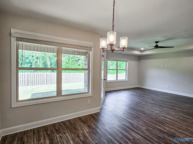 unfurnished room featuring a tray ceiling, ceiling fan with notable chandelier, baseboards, and dark wood-style flooring