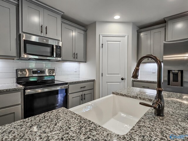 kitchen with light stone counters, a sink, gray cabinetry, stainless steel appliances, and tasteful backsplash