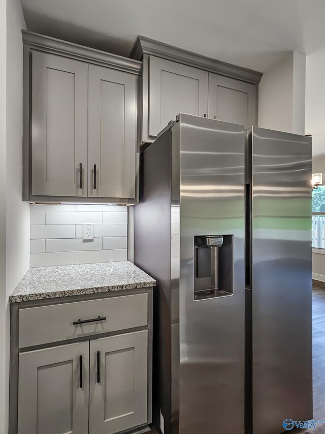 kitchen featuring backsplash, gray cabinetry, light stone counters, dark wood-style floors, and stainless steel fridge