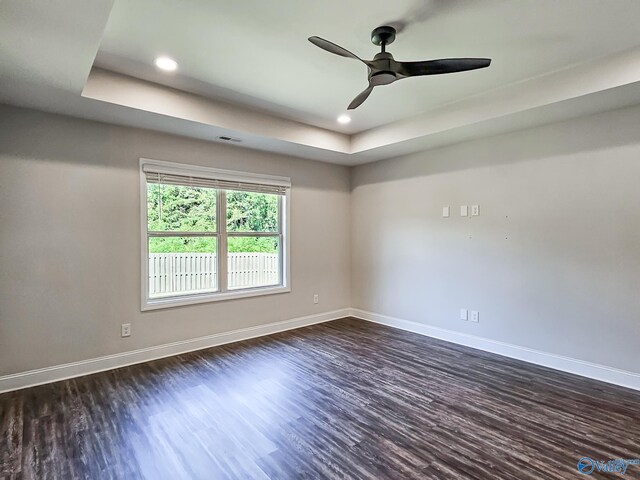 spare room with dark wood-type flooring, baseboards, recessed lighting, a raised ceiling, and a ceiling fan