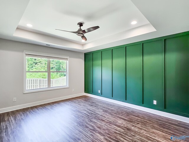 unfurnished room with a tray ceiling, dark wood-type flooring, a ceiling fan, and a decorative wall