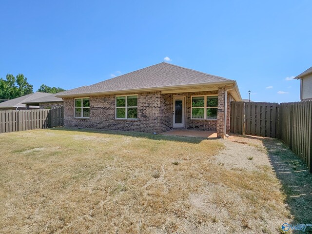 rear view of house with a fenced backyard, a lawn, brick siding, and roof with shingles