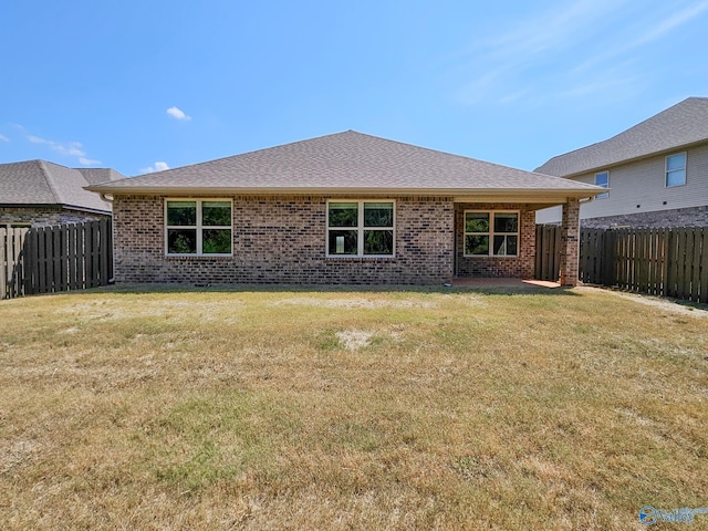 rear view of property featuring a yard, brick siding, and a fenced backyard