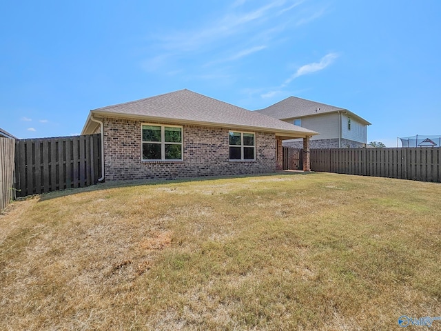 back of house featuring brick siding, a lawn, a shingled roof, and a fenced backyard