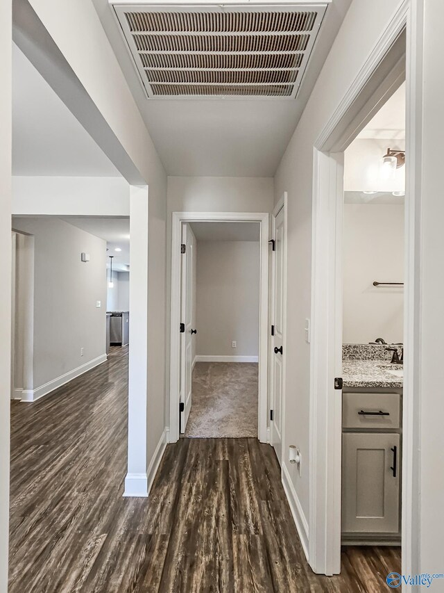 hallway featuring visible vents, dark wood-type flooring, and baseboards
