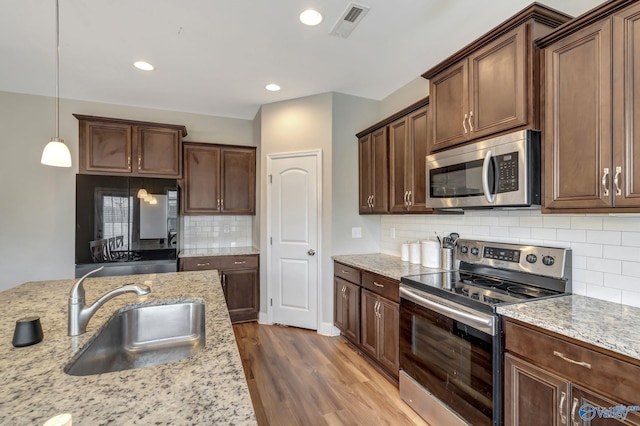 kitchen featuring appliances with stainless steel finishes, wood-type flooring, sink, hanging light fixtures, and light stone countertops