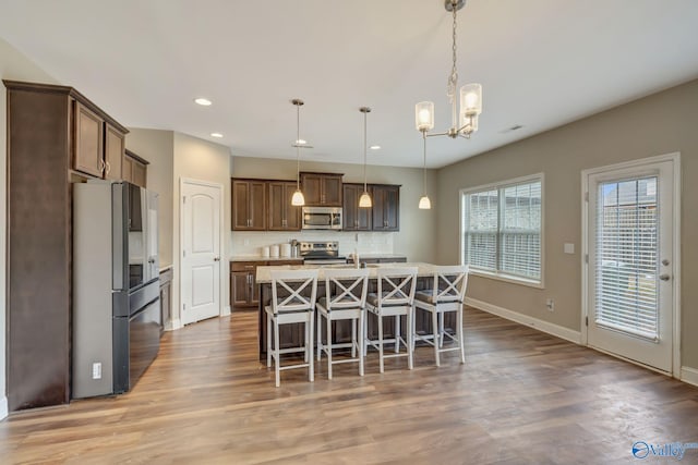 kitchen featuring an island with sink, a breakfast bar area, hanging light fixtures, stainless steel appliances, and light wood-type flooring