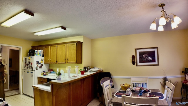 kitchen featuring kitchen peninsula, white fridge, a chandelier, pendant lighting, and a textured ceiling