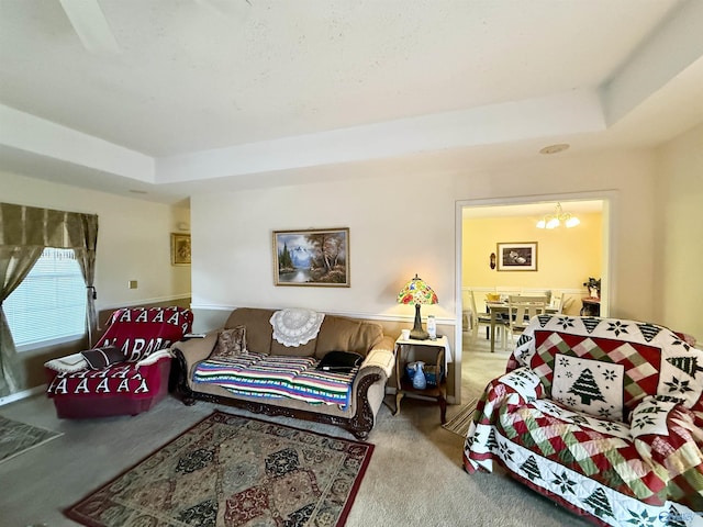 living room featuring a raised ceiling, carpet, and an inviting chandelier