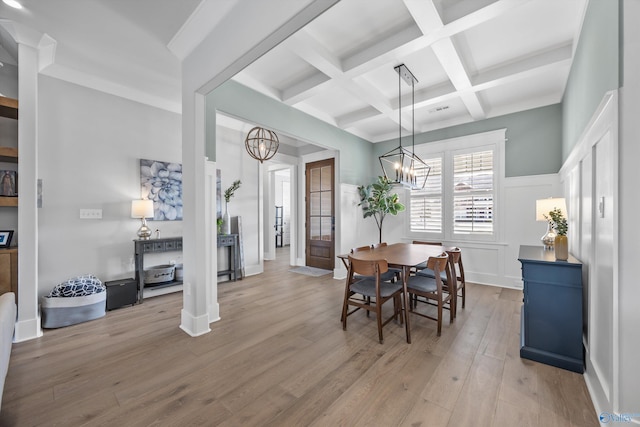 dining area with beam ceiling, a notable chandelier, light wood finished floors, coffered ceiling, and a decorative wall