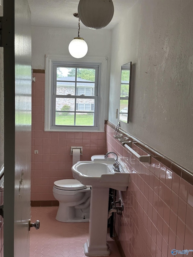 half bathroom featuring tile walls, toilet, a wainscoted wall, a textured wall, and tile patterned floors