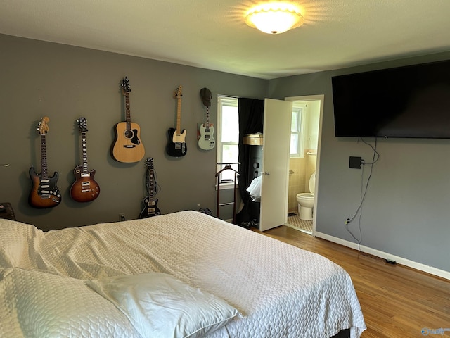 bedroom featuring wood finished floors, baseboards, and ensuite bath