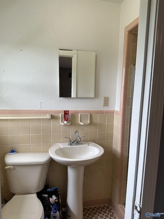 bathroom with tile walls, toilet, a stall shower, and a wainscoted wall
