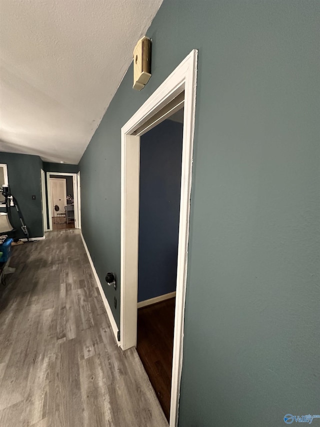 hall with wood finished floors, a textured ceiling, and baseboards