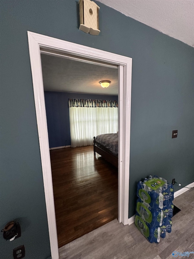 corridor featuring wood finished floors, baseboards, and a textured ceiling