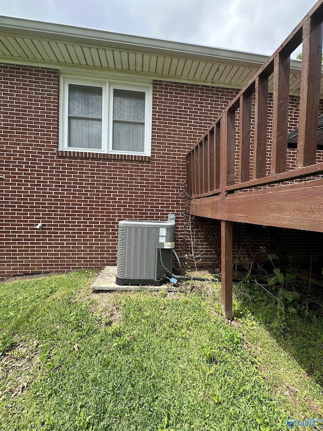 view of side of property with cooling unit, brick siding, a yard, and a deck