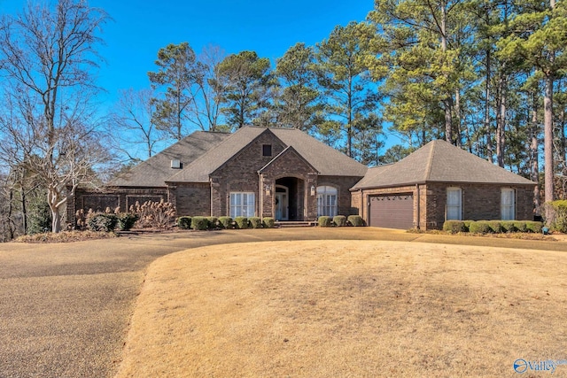 french country style house featuring a garage, brick siding, and roof with shingles