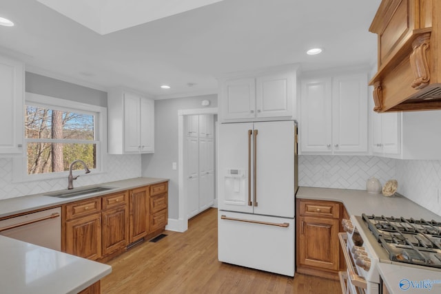 kitchen featuring white appliances, light wood-style flooring, a sink, light countertops, and white cabinets