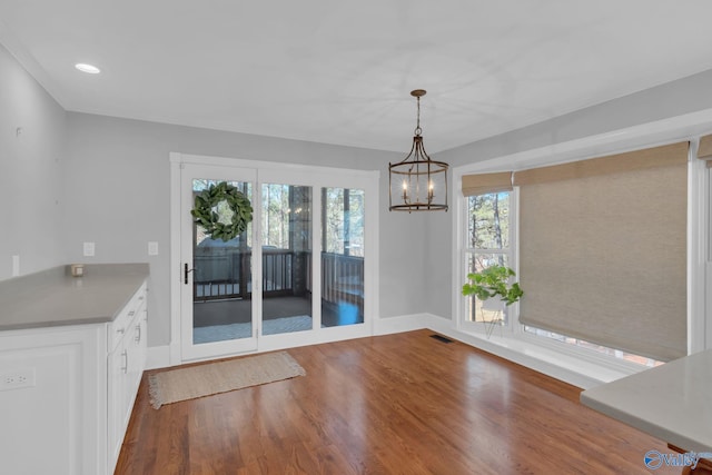 unfurnished dining area with visible vents, baseboards, recessed lighting, wood finished floors, and a notable chandelier