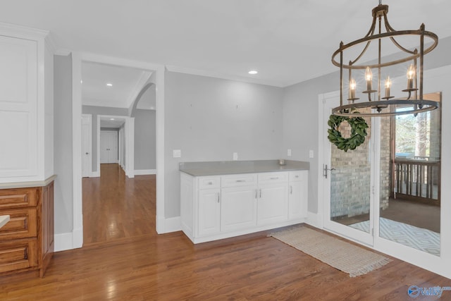 kitchen featuring white cabinets, wood finished floors, arched walkways, and ornamental molding