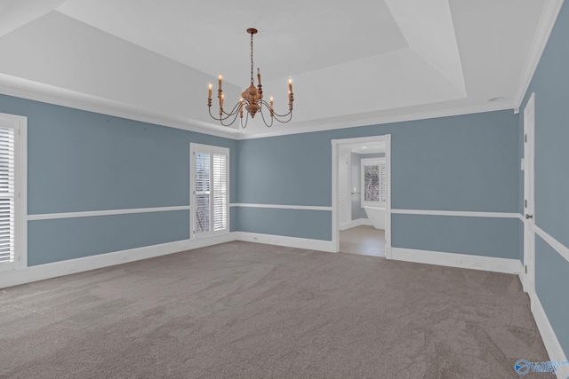 carpeted empty room with a tray ceiling, baseboards, a chandelier, and ornamental molding