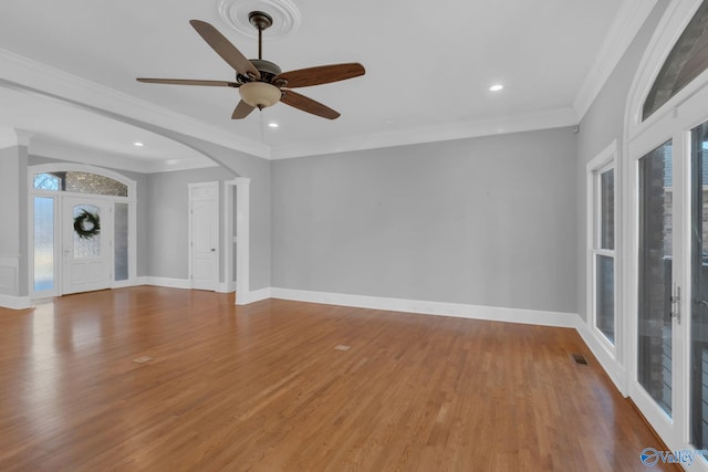 unfurnished living room featuring arched walkways, ornamental molding, baseboards, and wood finished floors