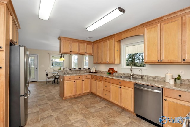 kitchen featuring light brown cabinets, light stone counters, appliances with stainless steel finishes, a peninsula, and a sink