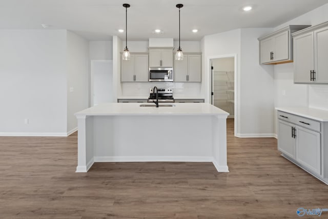 kitchen with gray cabinetry, hardwood / wood-style floors, a center island with sink, sink, and tasteful backsplash