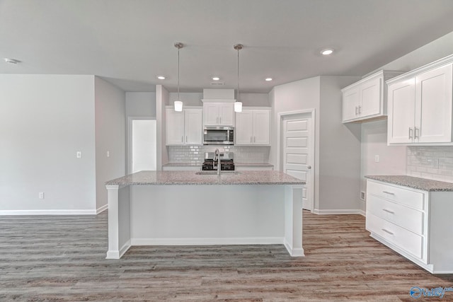 kitchen featuring white cabinetry, sink, light stone countertops, and a center island with sink