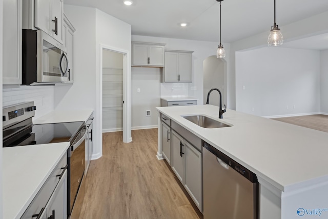 kitchen with backsplash, sink, hanging light fixtures, an island with sink, and stainless steel appliances