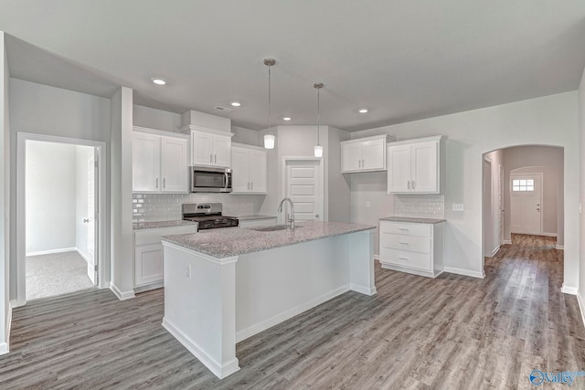 kitchen featuring white cabinetry, hanging light fixtures, stainless steel appliances, an island with sink, and light wood-type flooring