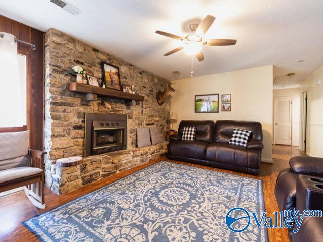 living room featuring a stone fireplace, ceiling fan, and hardwood / wood-style flooring