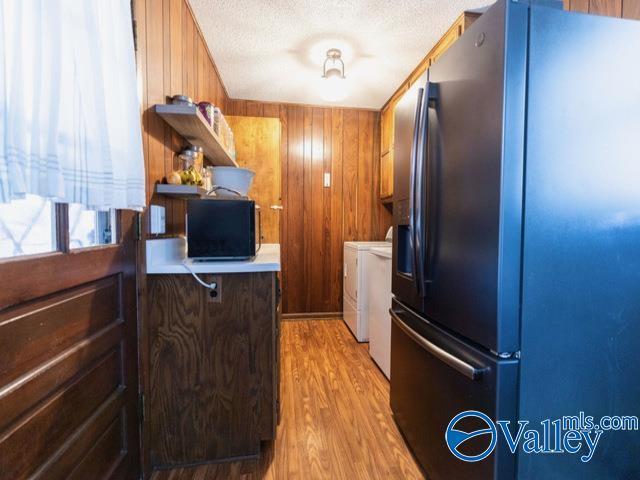 kitchen with washer and clothes dryer, wood walls, light hardwood / wood-style flooring, a textured ceiling, and stainless steel fridge with ice dispenser