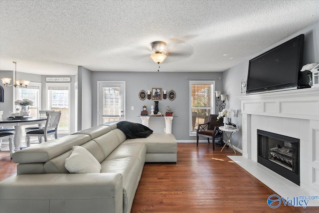 living room featuring dark hardwood / wood-style floors, a tiled fireplace, a textured ceiling, and ceiling fan with notable chandelier