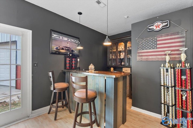 bar with light hardwood / wood-style flooring, hanging light fixtures, a textured ceiling, and wood counters