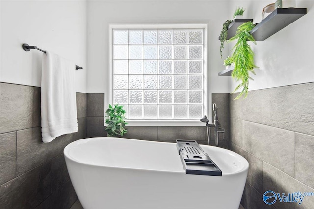 bathroom with a tub to relax in and tile walls