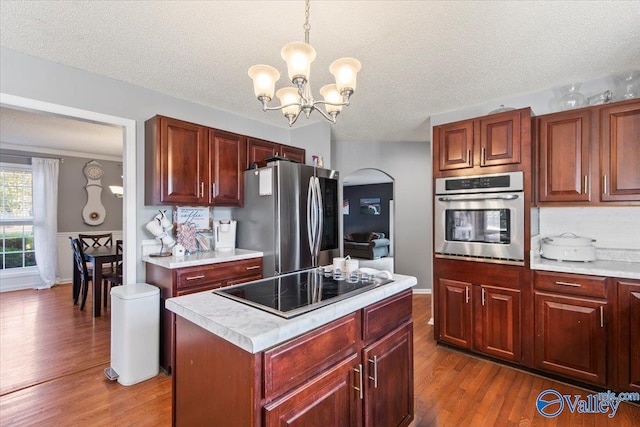 kitchen with hanging light fixtures, an inviting chandelier, dark hardwood / wood-style floors, stainless steel appliances, and a center island