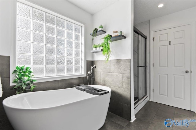 bathroom with a textured ceiling, plus walk in shower, tile patterned floors, and tile walls