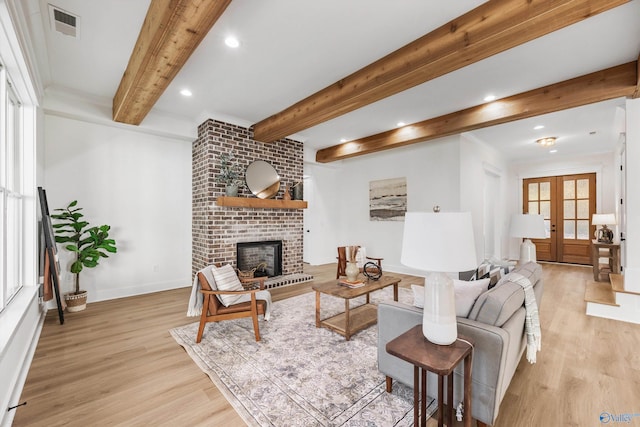 living room featuring french doors, beamed ceiling, light hardwood / wood-style flooring, crown molding, and a brick fireplace