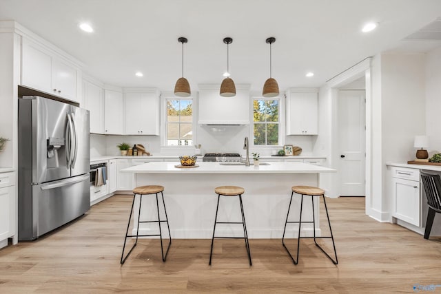 kitchen with appliances with stainless steel finishes, light hardwood / wood-style flooring, white cabinets, and a kitchen island with sink