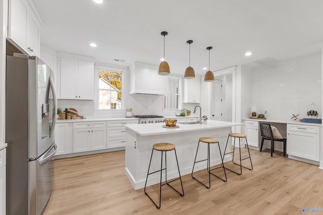 kitchen featuring hanging light fixtures, white cabinetry, a kitchen island with sink, light wood-type flooring, and stainless steel appliances