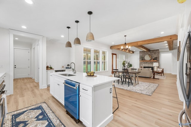 kitchen with hanging light fixtures, white cabinetry, a fireplace, light hardwood / wood-style floors, and sink