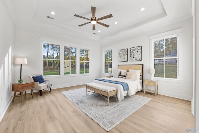 bedroom with ceiling fan, a tray ceiling, multiple windows, and light hardwood / wood-style floors