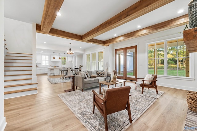 living room featuring beam ceiling, a chandelier, light hardwood / wood-style floors, and french doors