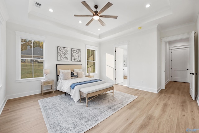 bedroom with a raised ceiling, ceiling fan, connected bathroom, crown molding, and light hardwood / wood-style flooring