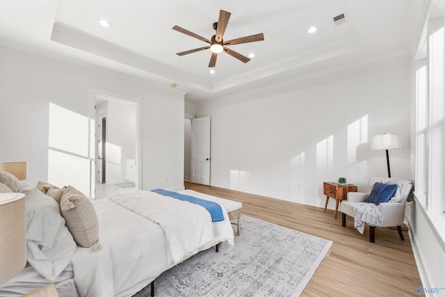 bedroom featuring light hardwood / wood-style flooring, a tray ceiling, ensuite bathroom, and ceiling fan